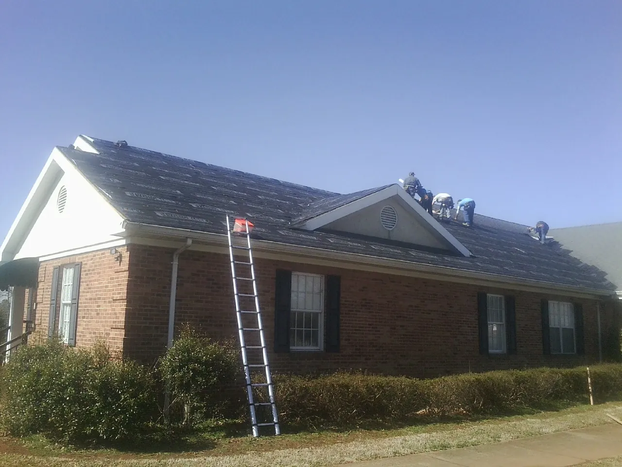 Crew tearing shingles off a brick ranch roof with a ladder set — Emergency Roof Repair work by our crew in South Kent