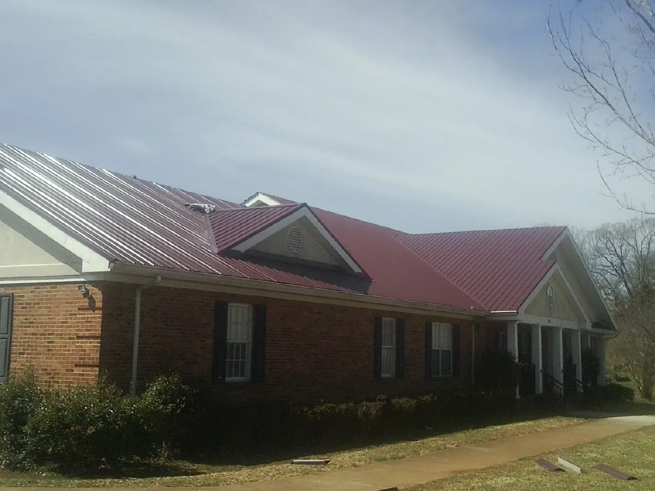 Red metal roof with gabled entries on a long brick building, from a Hail Damage Roof Repair job in South Kent