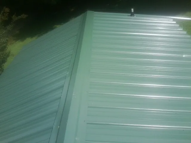 New green metal panels meeting at the ridge of a roof — Flat Roof Repair work by our crew in South Kent