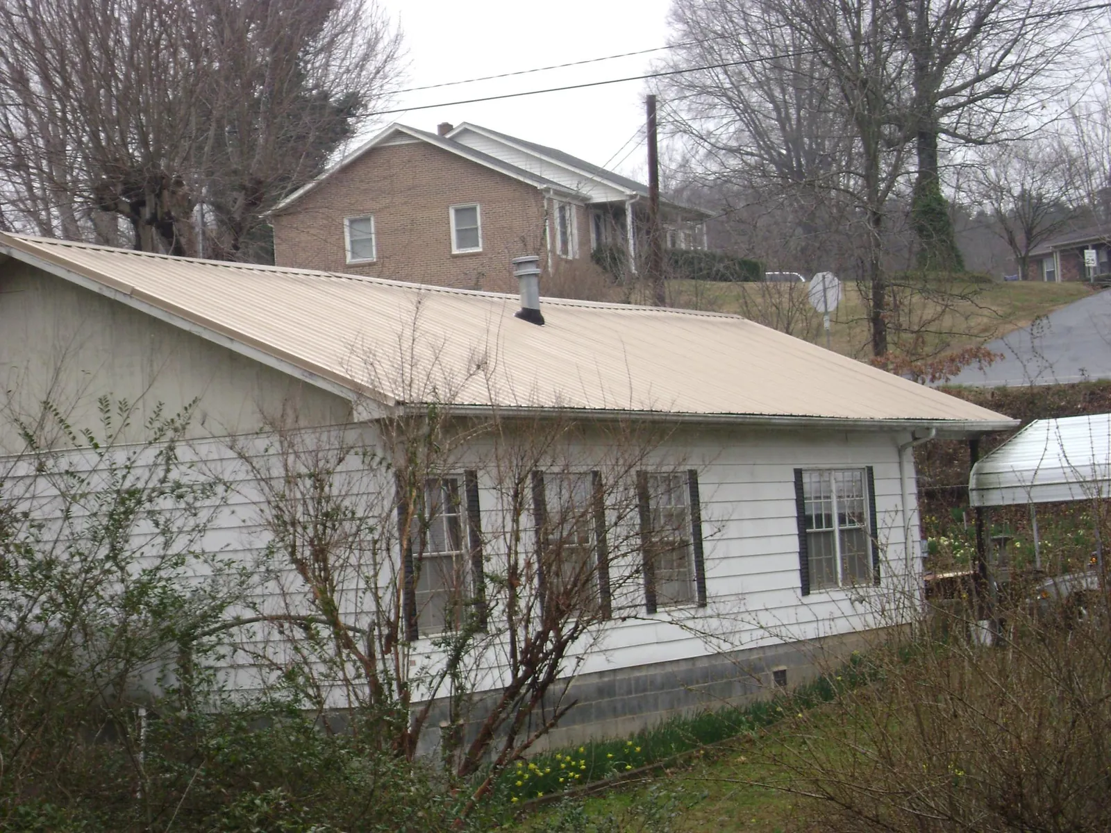 Tan metal roof on a white sided house set into a hillside — Commercial Roofing by Roofing Brothers in South Kent